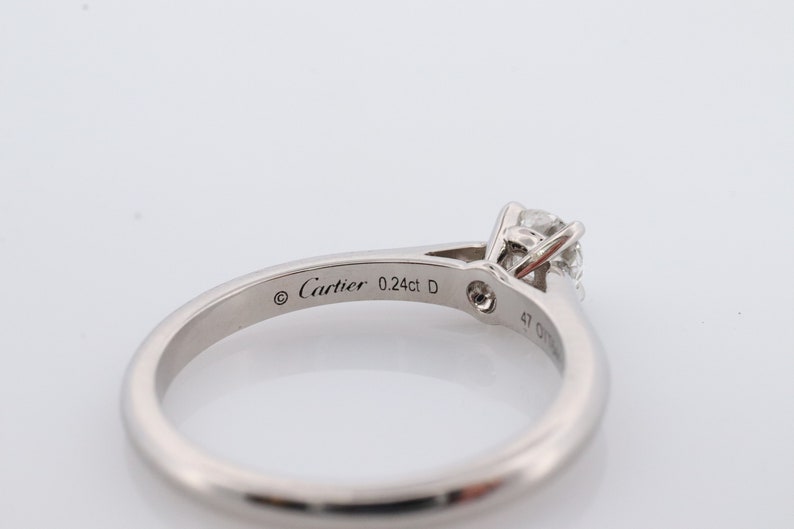 May include: A silver Cartier ring with a single round diamond. The ring is engraved with the words 'Cartier 0.24ct D'.