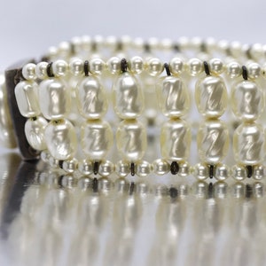 May include: A white pearl bracelet with a black leather closure. The bracelet is made of multiple strands of pearls and has a simple design.