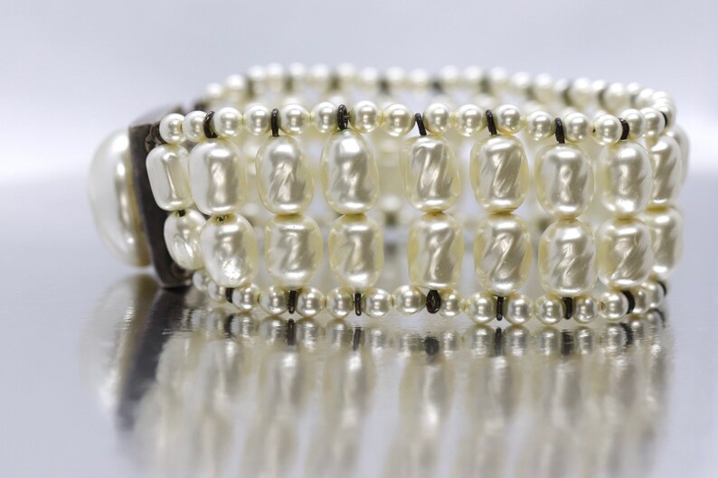 May include: A white pearl bracelet with a black leather closure. The bracelet is made of multiple strands of pearls and has a simple design.