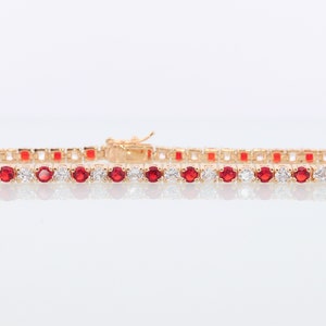May include: A gold tennis bracelet with alternating red and white round stones.