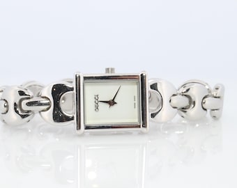 May include: A silver-toned Gucci watch with a square face and a white dial. The watch features black hands and the Gucci logo. The band is made of interlocking, rounded links.