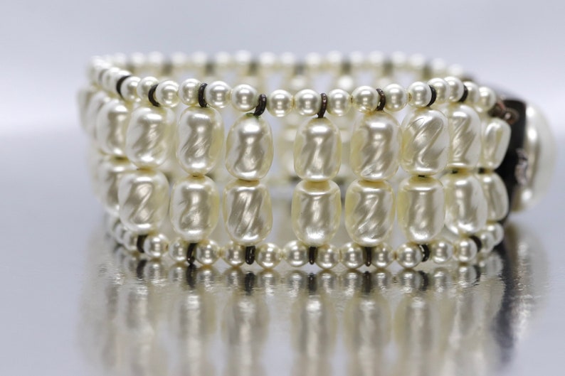 May include: A white pearl bracelet with multiple rows of pearls and a black clasp.