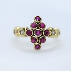 May include: A gold ring with a cluster of ruby stones set in a diamond shape. The ring has a band with smaller diamonds.