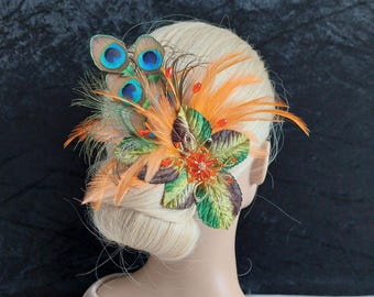 May include: A hair accessory featuring vibrant orange feathers, iridescent peacock feathers, and green fabric leaves. The centre is adorned with a small orange flower made of beads and sequins, with additional orange bead accents throughout.