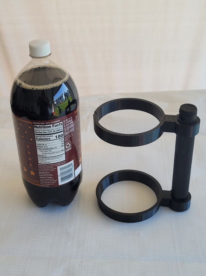 May include: A black plastic 2-bottle holder with a handle. The holder has two circular openings for bottles and a vertical handle. The holder is on a white surface.