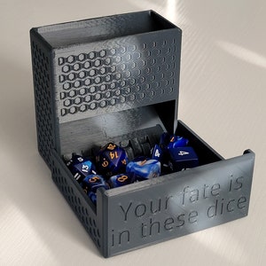 May include: A gray 3D-printed dice tower with a tray filled with blue and gold dice. The tower has a honeycomb pattern on the side and the text "Your fate is in these dice" on the front.