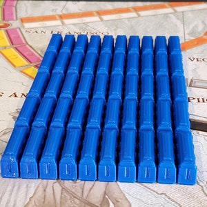 May include: A set of 40 blue plastic game pieces, each with a raised design resembling a building. The pieces are arranged in a rectangular formation.