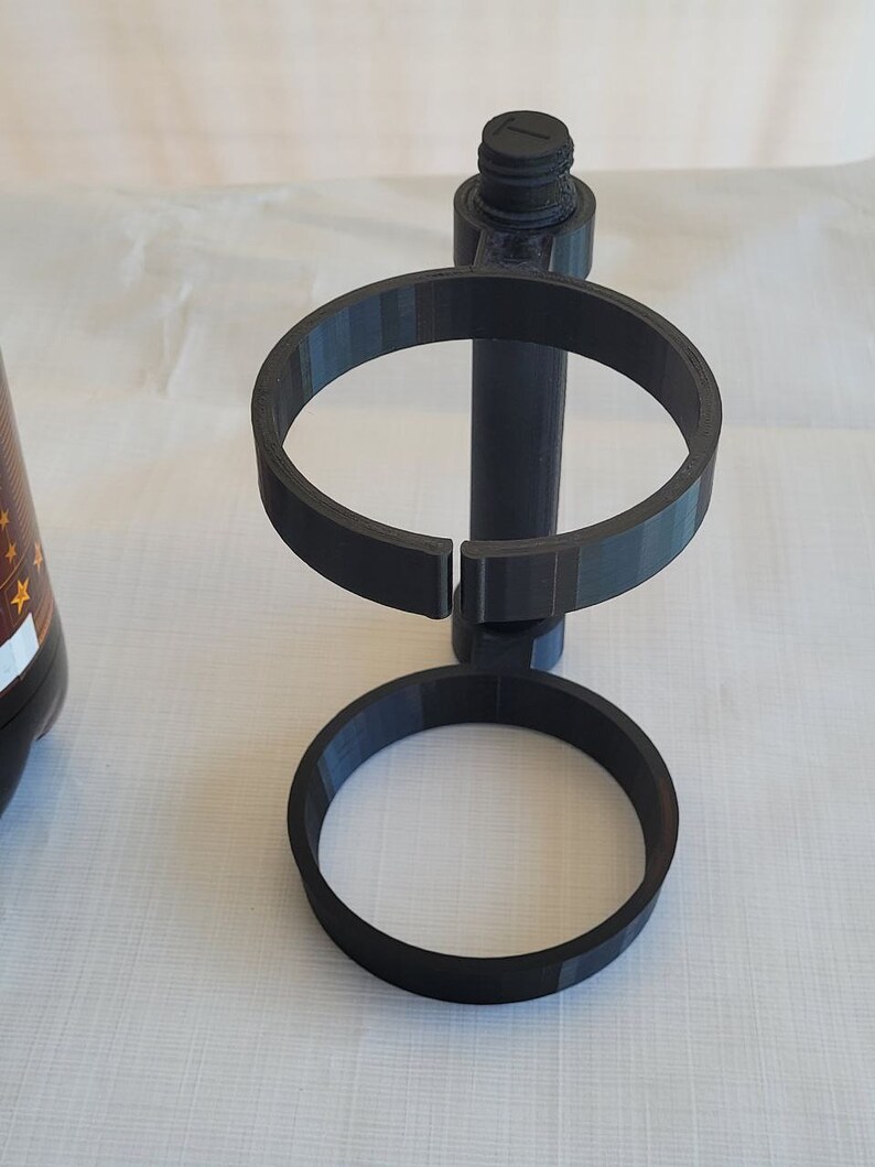 May include: A black 3D printed stand with two circular rings for holding bottles or cans.