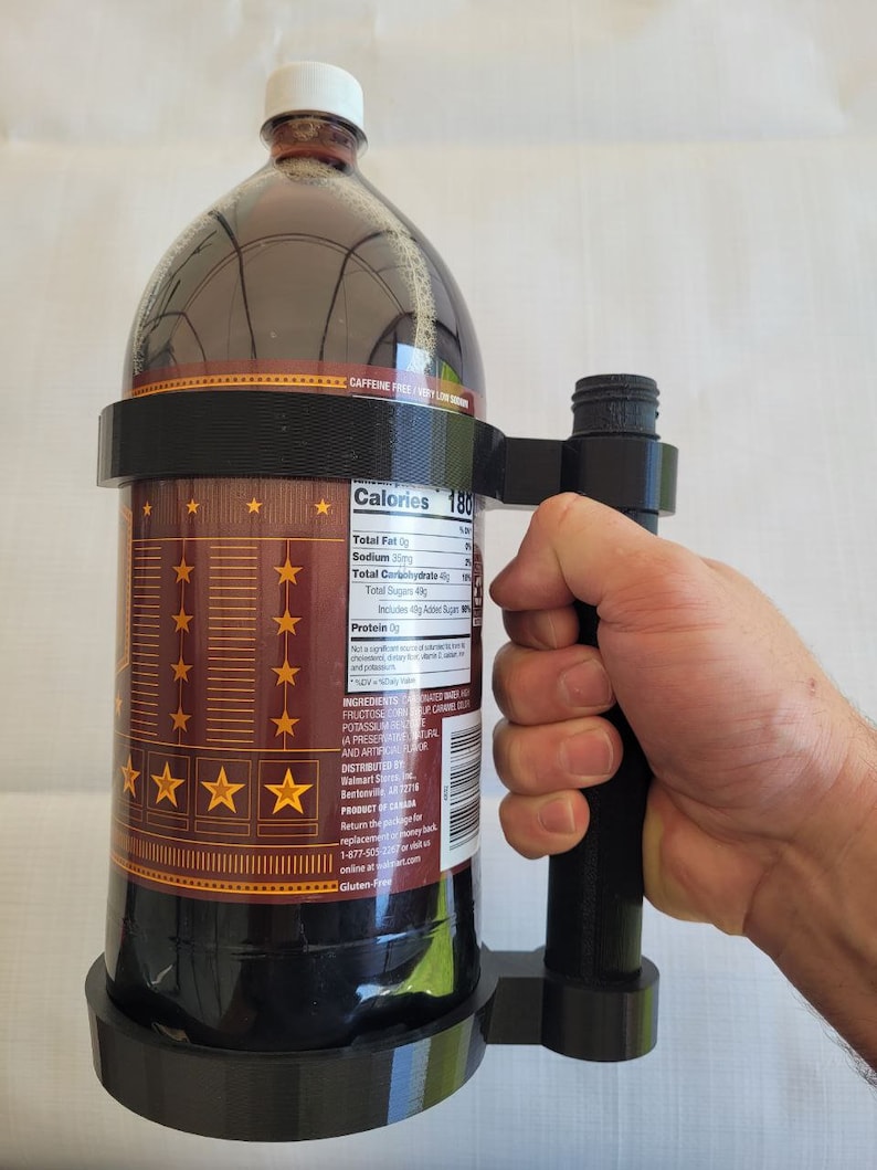 May include: A black plastic bottle holder with a handle. The holder is designed to hold a large bottle of soda or juice. The bottle is brown and has a label with nutritional information. The label includes the text "Calories 180".