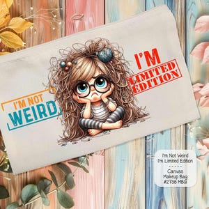 May include: A white canvas makeup bag with a cartoon illustration of a girl with messy hair and glasses. The bag has the text "I'm Not Weird I'm Limited Edition" printed on it.