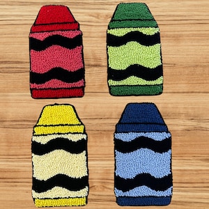 May include: Four colorful crayon-shaped decorative items. Each crayon has a different color: red, green, yellow, and blue. Each crayon has a black wavy design. The items are placed on a wooden surface.