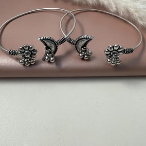 Peut inclure: Deux bracelets en argent avec un motif de croissant de lune et un motif floral. Les bracelets sont en métal et ont une finition argentée.