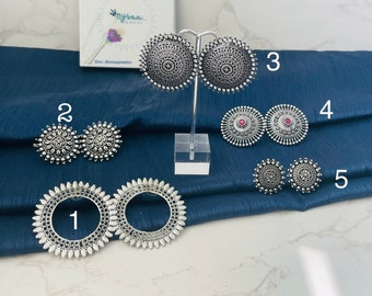 Pode incluir: Cinco pares de brincos de prata com designs diferentes. Os brincos são exibidos em um fundo de tecido azul. Os brincos são numerados de 1 a 5.