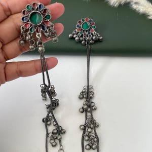 May include: A pair of silver-toned earrings. Each earring features a floral design with green, red, and blue accents. Dangling from the floral design are chains with small, round, silver-toned beads.