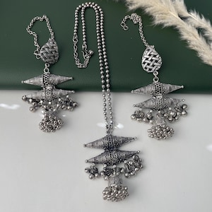 May include: Silver-toned jewelry set featuring a headpiece and two matching earrings. The pieces have intricate geometric designs and dangling bead clusters. The headpiece has a long chain of small beads. The earrings have a teardrop-shaped top.