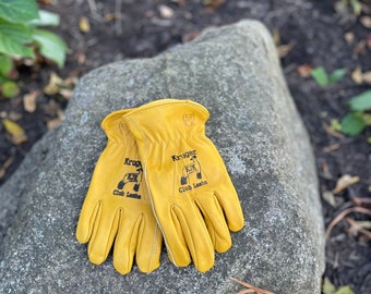 May include: A pair of yellow leather work gloves with the text "Kruger Club Lambs" embroidered on the back of each glove.