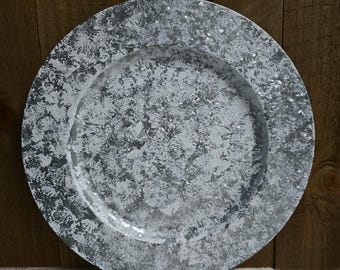 May include: A round, decorative charger plate with a metallic silver finish and a distressed, speckled white overlay. The plate has a wide rim and is suitable for serving or display. The plate is approximately 12 inches in diameter.
