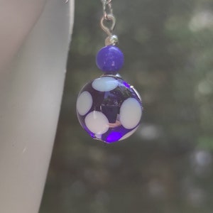 Peut inclure: Boucles d'oreilles pendantes en verre à pois violets et blancs avec crochets argentés.