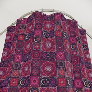 May include: A patterned shower curtain with a repeating design of squares in shades of pink, purple, and red. Each square features a floral or geometric pattern, with crescent moon accents. The curtain hangs from a curved metal rod.