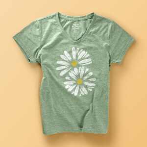 May include: A green t-shirt with a white daisy print. The shirt has a V-neck and short sleeves.