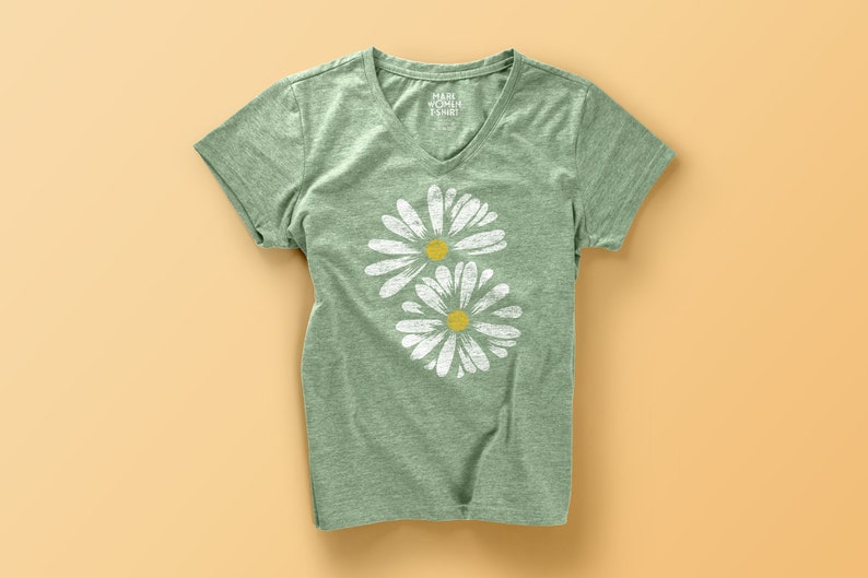 May include: A green t-shirt with a white daisy print. The shirt has a V-neck and short sleeves.