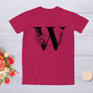 May include: A pink t-shirt with a black floral design featuring the letter "W".