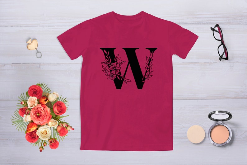 May include: A pink t-shirt with a black floral design featuring the letter "W".