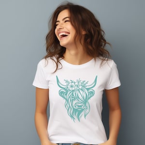 May include: A white t-shirt with a teal floral design of a Highland cow's head.