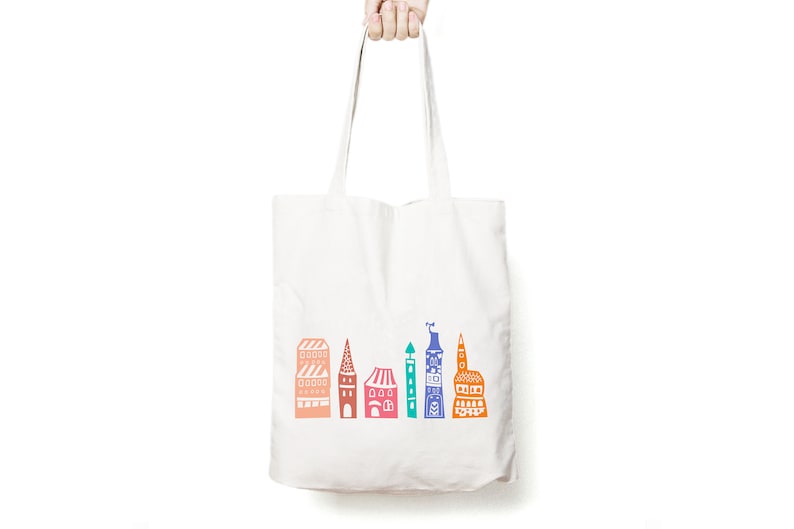 May include: White canvas tote bag with a colorful illustration of a city skyline. The buildings are in shades of orange, pink, blue, green, and purple.