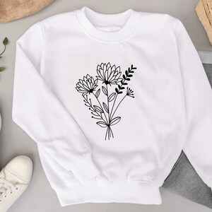 Pode incluir: Camisola branca com um desenho de linha preta de um buqu&ecirc; de flores na frente.