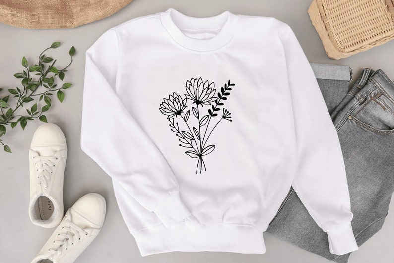 Pode incluir: Camisola branca com um desenho de linha preta de um buqu&ecirc; de flores na frente.