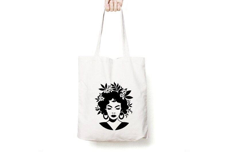 May include: A white tote bag with a black silhouette of a woman with flowers in her hair. The woman is wearing large earrings.