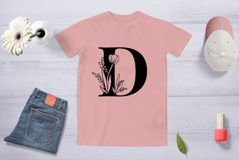 May include: A pink t-shirt with a black letter D and floral design. The letter D is outlined in black and filled in with black. The floral design is black and features a tulip and leaves.