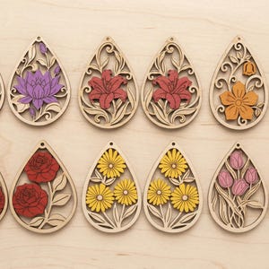 May include: A collection of wooden teardrop-shaped earrings with floral designs. The earrings feature various flowers, including lotuses, lilies, daisies, roses, and tulips, in shades of purple, red, yellow, orange, and pink. The earrings are laser-cut with intricate details.