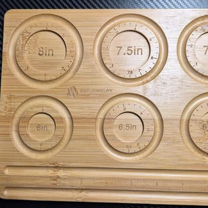 May include: A bamboo ring sizer with six circular measuring guides labeled 6in, 6.5in, 6.75in, 7in, 7.5in, and 8in. The board also includes a ruler along the bottom and the text "BBE JEWELRY".