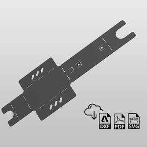 Puede incluir: Un objeto plano, rectangular y gris con un diseño recortado. El objeto tiene una forma larga y estrecha con dos extremos redondeados. El objeto está diseñado para ser doblado en una caja.