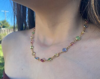 May include: A gold chain necklace with oval-shaped gemstones in various colors, including pink, green, blue, and yellow.