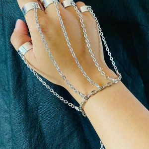 May include: A silver chain bracelet with multiple rings attached to the chain. The bracelet has a small silver charm at the end of the chain.