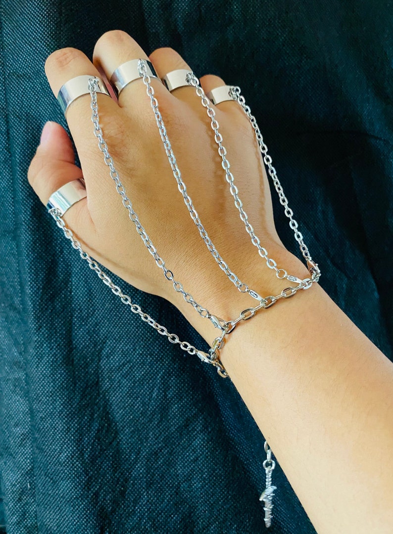 May include: A silver chain bracelet with multiple rings attached to the chain. The bracelet has a small silver charm at the end of the chain.
