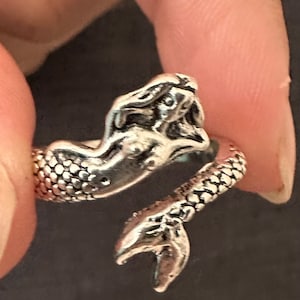 May include: Silver mermaid ring with a detailed design. The mermaid's tail is curled around the ring band.