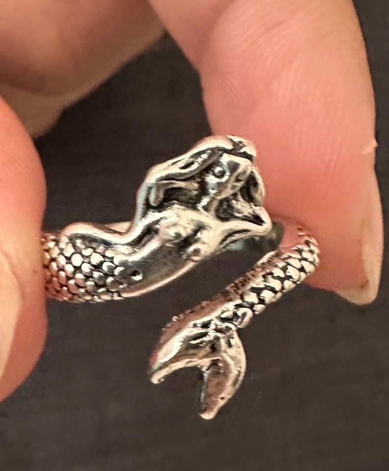 May include: Silver mermaid ring with a detailed design. The mermaid's tail is curled around the ring band.