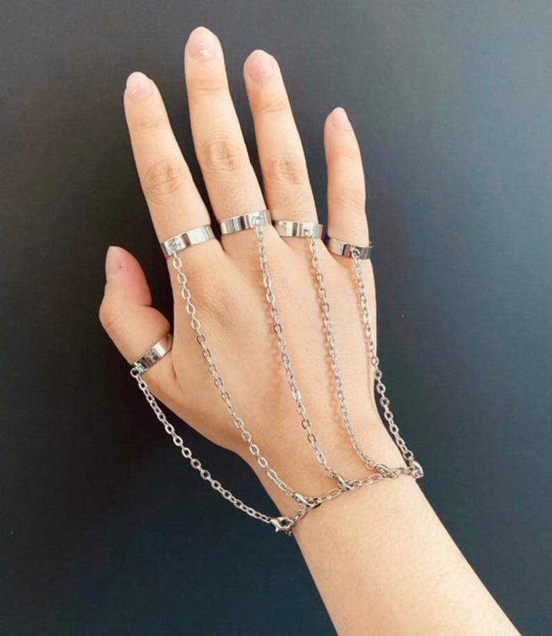 K&ouml;nnte beinhalten: Ein silbernes Kettenarmband mit mehreren Ringen, die an der Kette befestigt sind. Die Ringe sind durch Ketten miteinander verbunden, wodurch ein mehrschichtiger Look entsteht.