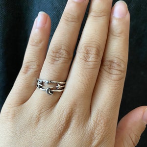 Könnte beinhalten: Ein silberner Ring mit einem Design aus Halbmond und Sternen. Der Ring wird am Mittelfinger einer Hand getragen.
