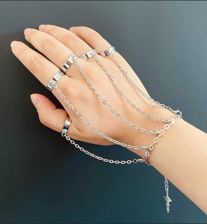 K&ouml;nnte beinhalten: Silbernes Kettenarmband mit mehreren daran befestigten Ringen. Das Armband hat einen kleinen silbernen Anh&auml;nger am Ende der Kette.