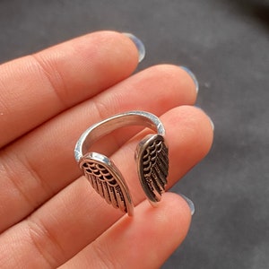 May include: A silver ring with two open wings on the band. The wings have a detailed design.