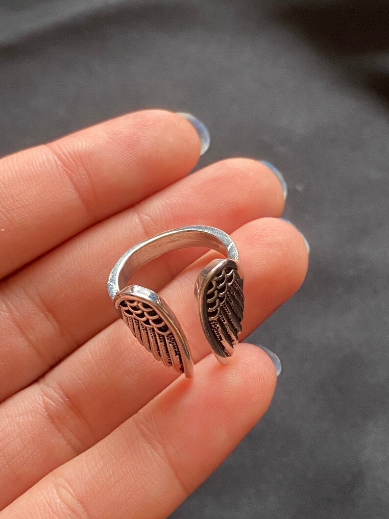 May include: A silver ring with two open wings on the band. The wings have a detailed design.