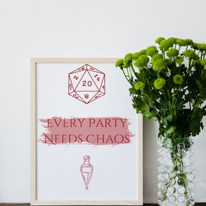 May include: A framed print with a red 20-sided die and the text "EVERY PARTY NEEDS CHAOS" in red with a pink brushstroke effect. A small vial with a cork is below the text. The print is on a wooden table with a vase of green flowers to the right.