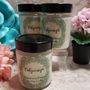 May include: Three glass jars with black lids containing soy candles. The jars have a green and white label with the text "Polymorph" and "Messosaurus Designs Pure Soy Candles".