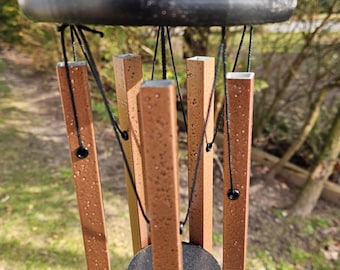 May include: A brown metal wind chime with six tubes hanging from a black metal ring. The tubes are suspended by black cords and have a textured surface. The wind chime is hanging outdoors.