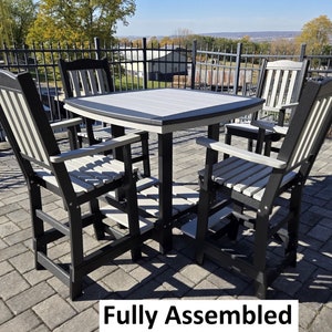 May include: A black and white outdoor dining set with a square table and four chairs. The table and chairs are made of weather-resistant plastic. The set is fully assembled.  "Fully Assembled" is written in white text on a black background.